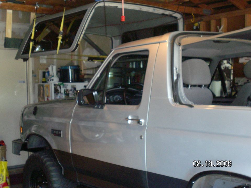 Silver Ford Bronco in garage with hardtop removed and hoisted on yellow ceiling straps