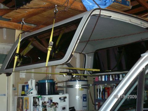 1996 Ford Bronco - A truck cap is suspended by chains and straps in a garage, with household items in the background.