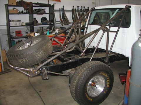 1984 Ford Bronco - Custom off-road truck chassis in a workshop, a roll cage and spare tire.