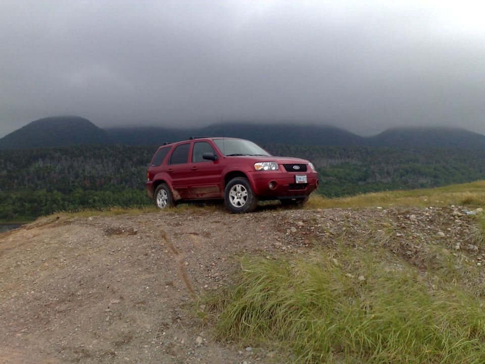 Red 2006 Ford Escape parked on a dirt hill with mountains in the background