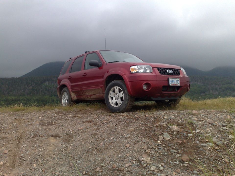 Red 2006 Ford Escape parked on a dirt hill with trees and mountains in the background