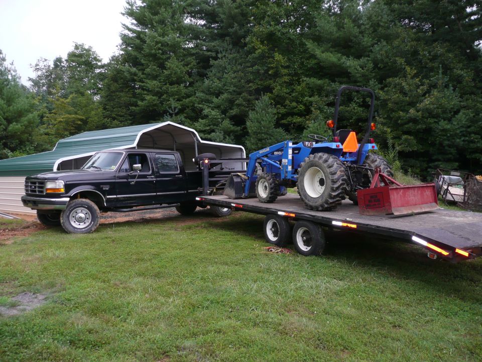 1997 Ford F-350 crew cab dually pickup truck towing a flatbed trailer with a blue tractor on it