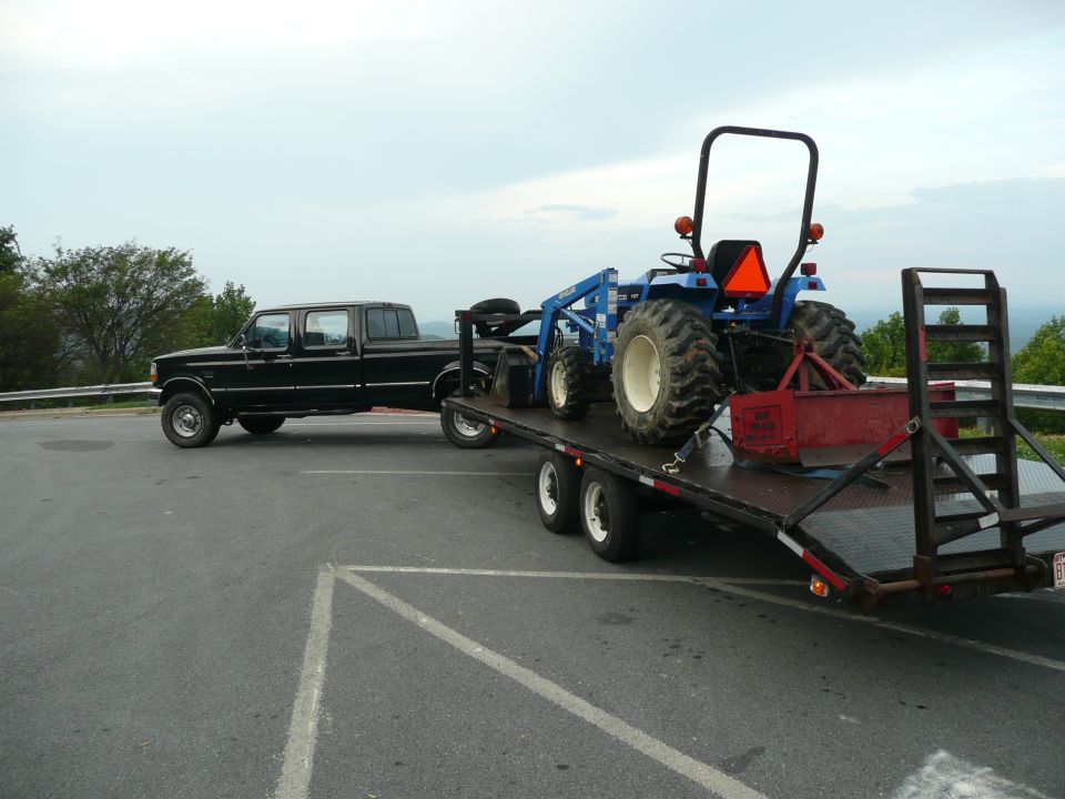 1997 Ford F-350 crew cab pickup truck towing a flatbed trailer with a blue tractor