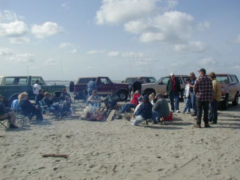 1989 Ford F-150 - A group enjoys a beach bonfire with several vehicles parked nearby under a cloudy sky.
