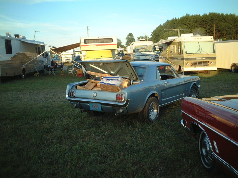 Light blue vintage Mustang coupe, trunk open full of firewood, at an RV campground.