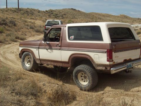 1985 Ford Bronco - This two-tone Ford Bronco is seen off-road, with another vehicle in the background.