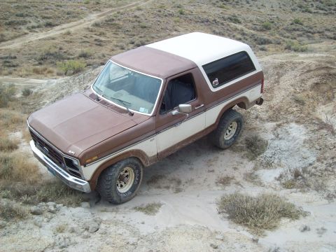 1985 Ford Bronco - This two-tone Ford Bronco is parked on a dirt path in a dry, hilly area.