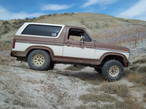 1985 Ford Bronco - This two-tone Ford Bronco navigates a dusty, arid landscape under a bright blue sky.