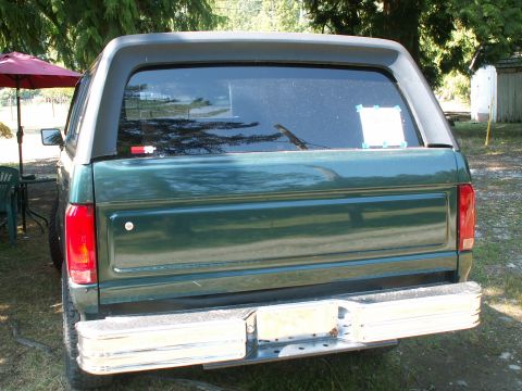 1990 Ford Bronco - The rear of a green SUV is shown parked outdoors with trees in the background.