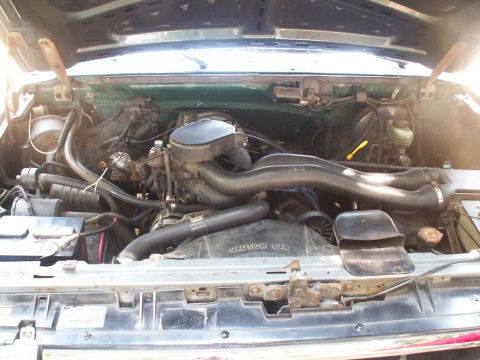 1990 Ford Bronco - The engine bay of a green vehicle is shown with the hood open, revealing the V8 engine and associated components.
