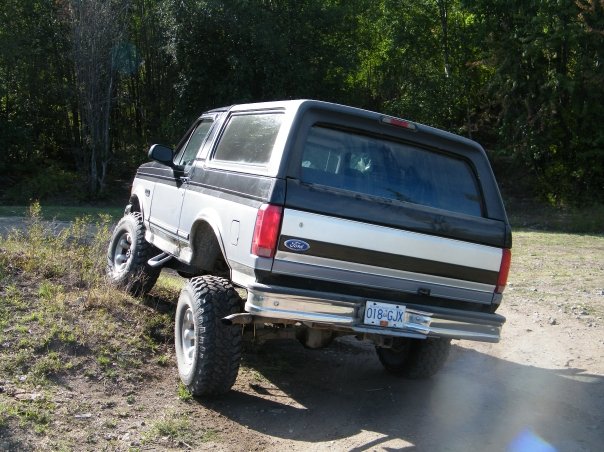 Lifted black-and-white Ford Bronco SUV on big mud tires, rear view on dirt lot