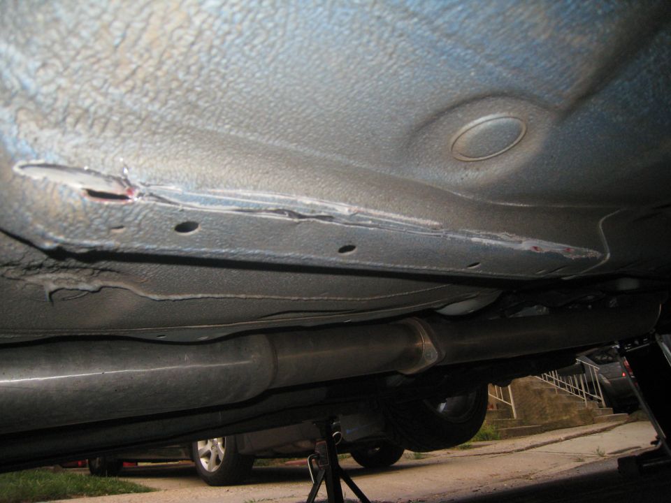 Underside of a car showing damage to the frame rail and exhaust system