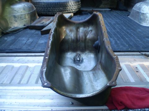 1979 Ford Bronco - An oil pan rests in the bed of a truck, next to a spare tire and a red cloth.