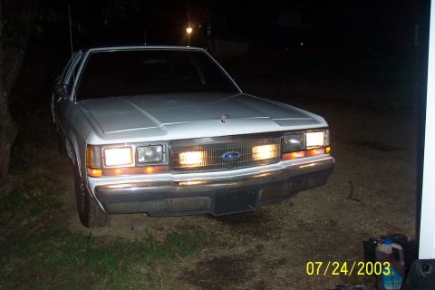 1991 Ford Crown Victoria LTD - Front view of a white 1991 Ford Crown Victoria LTD, with its driving lights and grille lit up at night.