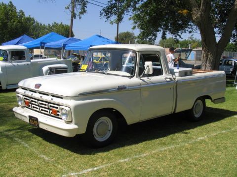 1984 Ford Bronco - A classic white Ford F-100 pickup truck is displayed outdoors with tents and other vehicles in the background.