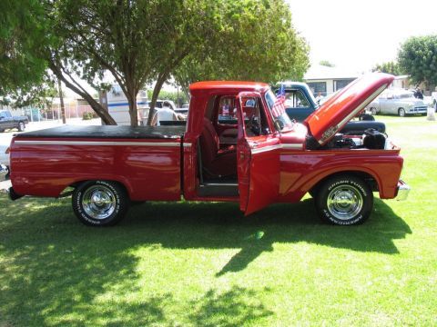 1984 Ford Bronco - This red pickup truck, likely from the early 1960s, is displayed outdoors with its hood and door open.