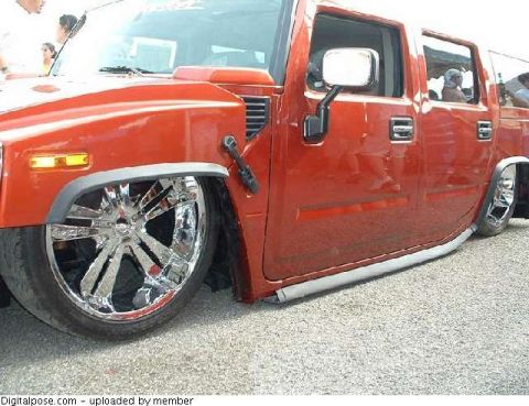 1990 Ford Bronco - Low close-up of the driver's side of an orange Hummer H2 aired out on the pavement, body dropped over huge chrome multi-spoke wheels with s…