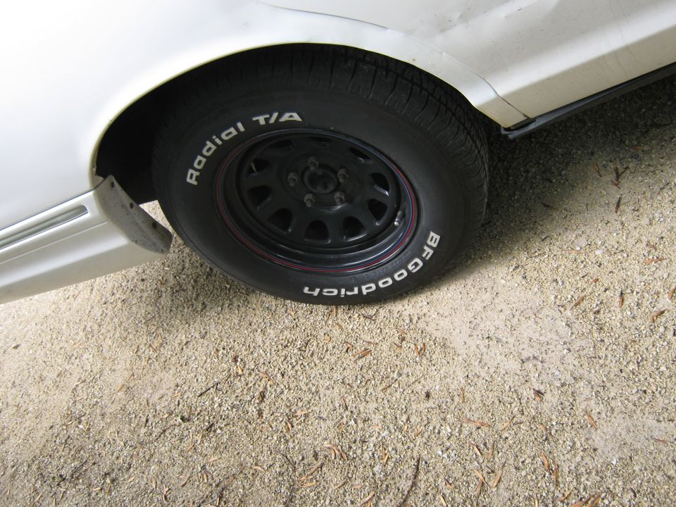 Black steel wheel with BFGoodrich Radial T/A white-letter tire on white sedan over gravel