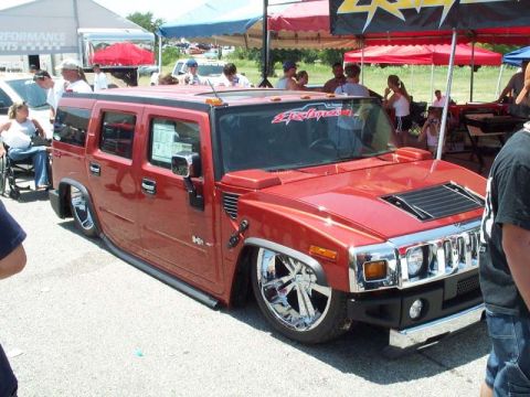 1990 Ford Bronco - A candy-red Hummer H2 slammed to the ground on air suspension, sitting on large polished chrome multi-spoke wheels with body-side step bars…