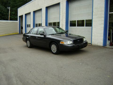 2001 Ford Crown Victoria - A dark gray 2001 Ford Crown Victoria is parked outside a commercial building with multiple garage bays.