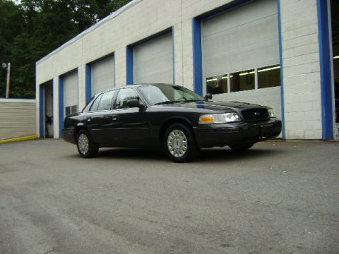 2001 Ford Crown Victoria - A dark gray 2001 Ford Crown Victoria is parked outside a building with multiple garage doors.