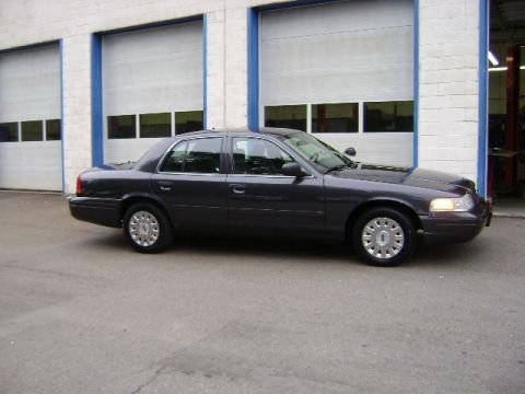 2001 Ford Crown Victoria - Side view of a dark gray 2001 Ford Crown Victoria sedan parked in front of a building with garage doors.