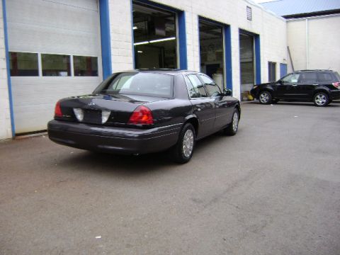 2001 Ford Crown Victoria - A dark gray 2001 Ford Crown Victoria sedan is parked outside a garage with another SUV in the background.