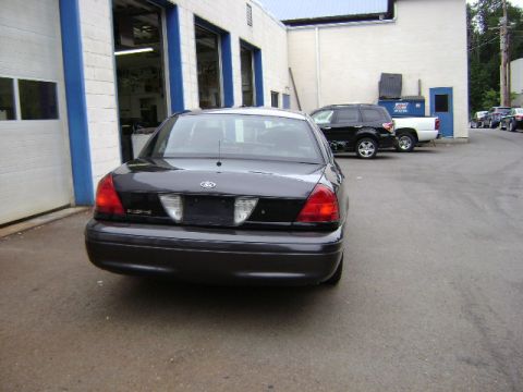 2001 Ford Crown Victoria - This dark gray 2001 Ford Crown Victoria is seen from the rear, parked outside a commercial building with other vehicles nearby.