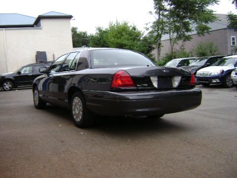 2001 Ford Crown Victoria - The rear of a black 2001 Ford Crown Victoria is shown parked in a lot with other vehicles.