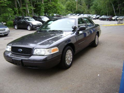 2001 Ford Crown Victoria - A dark gray 2001 Ford Crown Victoria is parked in a lot with trees and other vehicles in the background.