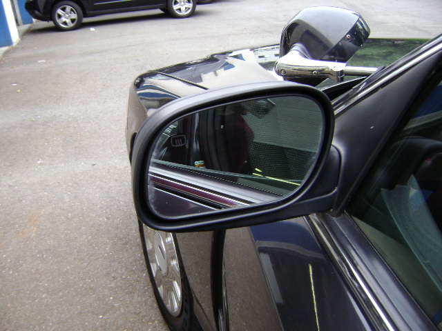 Side view of a dark police car with a spotlight mounted above the side mirror. Another dark SUV is parked behind it