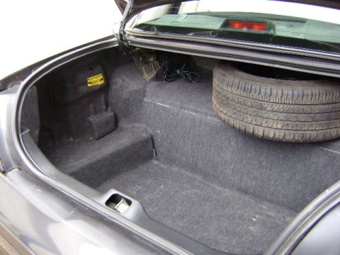 2001 Ford Crown Victoria - The trunk of a dark gray vehicle contains a spare tire and is lined with carpet.