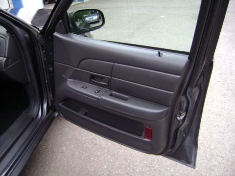 2001 Ford Crown Victoria - The interior door panel of a dark gray vehicle is visible, with a reflection of another car in the side mirror.