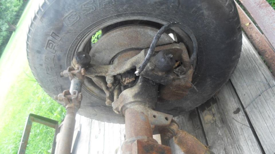 Close-up of rusty vehicle suspension and tire on wooden planks