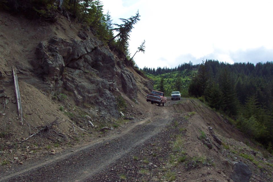 Red and white trucks parked on a gravel mountain logging road cut into a rocky hillside