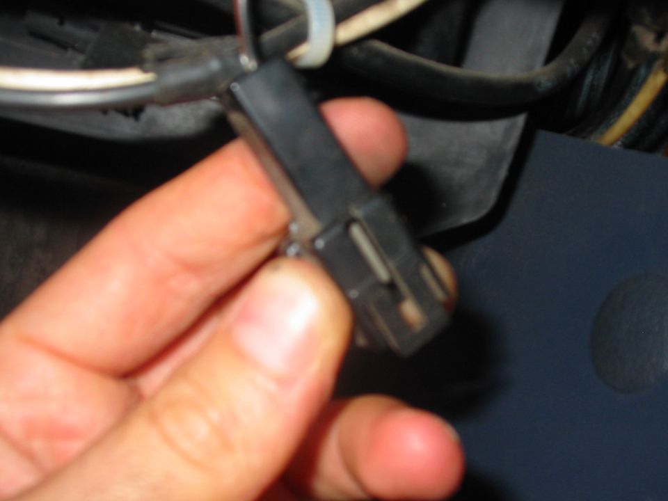 Hand holding a black automotive electrical connector near wiring harness