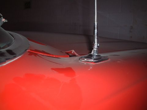 1967 Ford Galaxie - Close-up of a chrome antenna base and hood ornament on a red vehicle.