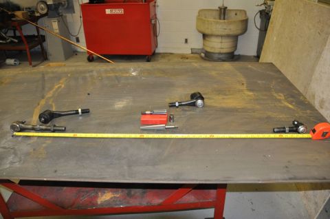 1996 Ford Bronco - Tie rod ends and a measuring tape are displayed on a workbench in a workshop setting.