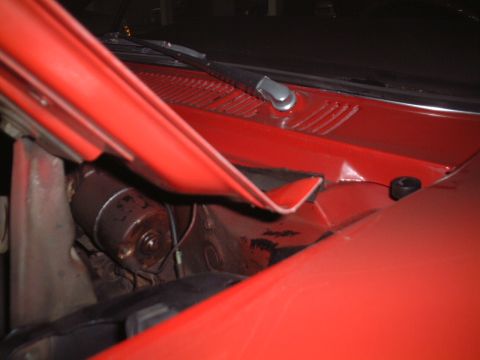 1967 Ford Galaxie - Close-up of the cowl area under the hood of a red car, revealing the windshield wiper motor.