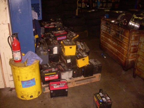 1993 Ford Bronco - A collection of used car batteries are stacked on a wooden pallet in a workshop setting.
