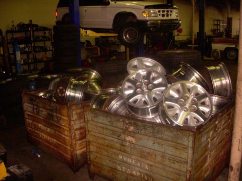 1993 Ford Bronco - A white 1995 Ford Explorer is elevated on a lift in a garage, with several bins of alloy wheels visible in the foreground.