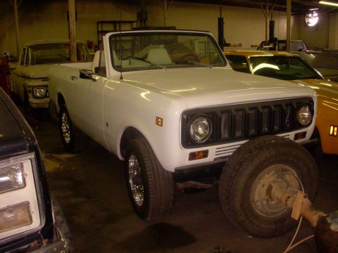 1993 Ford Bronco - A white convertible SUV is parked in a garage with a spare tire in front of it.