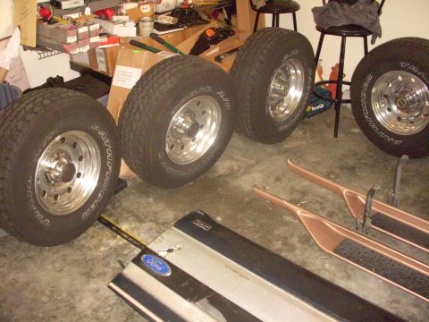 1993 Ford Bronco - Parts laid out on a garage floor, including tires, rims, running boards, and a Ford emblem.