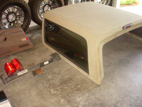 1993 Ford Bronco - A detached tan hardtop for a Ford Bronco sits on a concrete floor with various vehicle parts nearby.