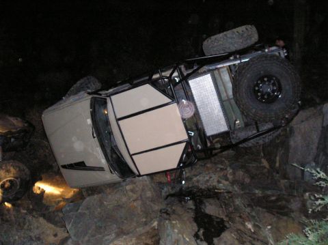 1986 Toyota Hilux - This modified off-road vehicle is resting on its side amidst rocks, illuminated by its headlights.