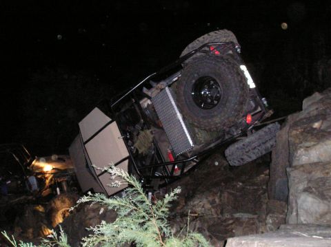 1986 Toyota Hilux - An off-road vehicle is seen tipped onto its side amidst rocks and darkness, with another vehicle visible in the background.