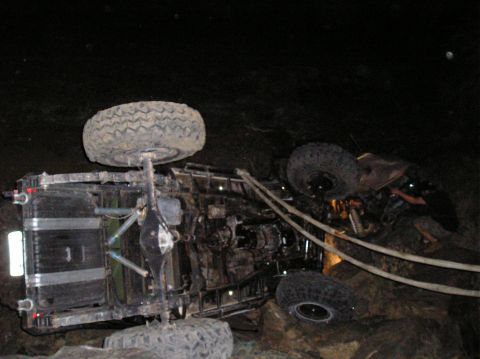 1986 Toyota Hilux - An off-road vehicle has rolled onto its side in a challenging terrain at night.