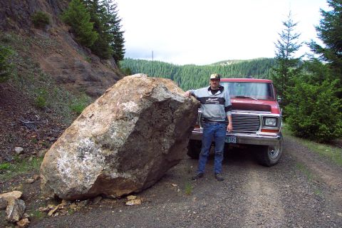 1989 Ford F-150 - A man poses with a large boulder and a red pickup truck on a dirt road.
