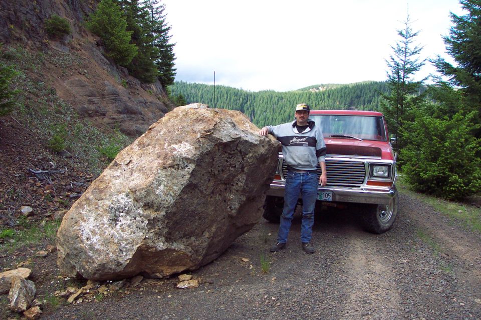 Man beside boulder on gravel road with red Ford pickup and Oregon plate