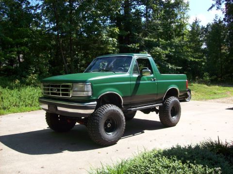 1992 Ford Bronco - This lifted green Ford Bronco is shown from a three-quarter front view, parked outdoors on a paved surface.